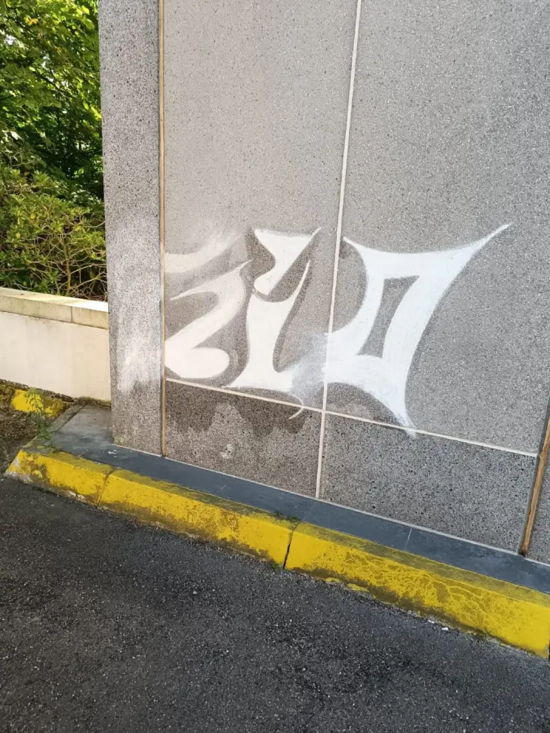 Graffiti partiellement effacé sur mur en pierre grâce à un nettoyage adapté sans abîmer le support
